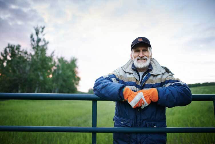 A man wearing a coat and gloves leans over a gate.